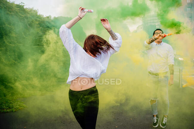 Grupo de amigos de raza mixta pasando el rato juntos en la ciudad, usando coloridas bombas de humo. - foto de stock