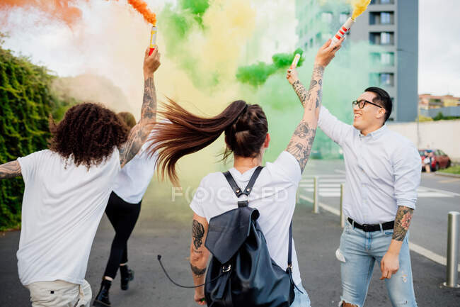 Gemischte Rassengruppe von Freunden, die gemeinsam in der Stadt abhängen, mit bunten Rauchbomben. — Stockfoto