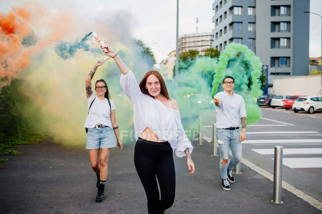Gruppo misto di amici che escono insieme in città, usando bombe fumogene colorate. — Foto stock