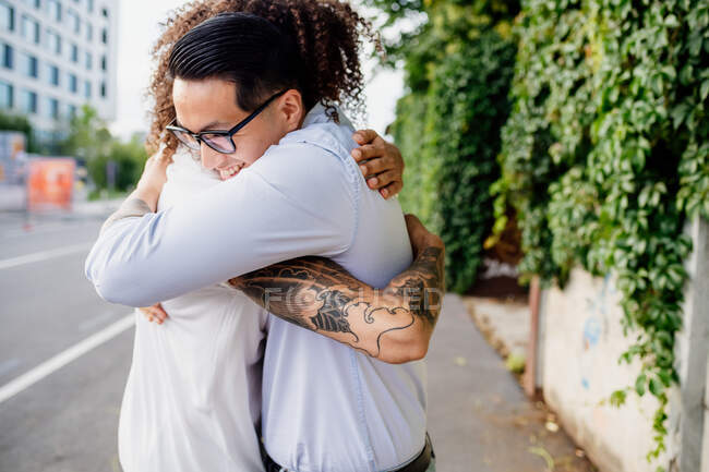 Two men with tattooed arms standing on sidewalk, hugging. — Stock Photo