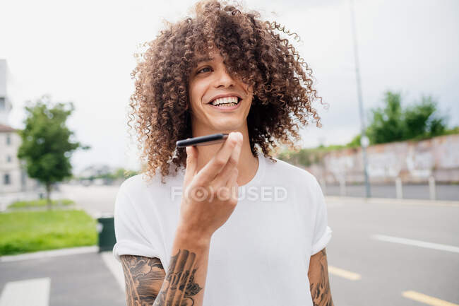 Portrait d'homme aux bras tatoués et aux longs cheveux bouclés bruns, à l'aide d'un téléphone portable. — Photo de stock