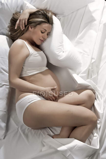 Portrait of heavily pregnant woman lying on bed, cradling stomach. — Stock Photo