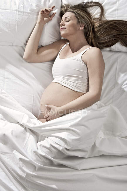 Retrato de mulher fortemente grávida deitada na cama, embalando o estômago. — Fotografia de Stock