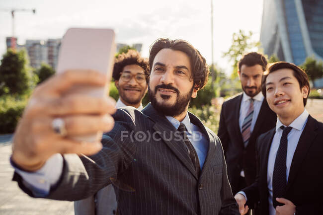 Groupe mixte d'hommes d'affaires traînant ensemble en ville, prenant selfie avec téléphone portable. — Photo de stock