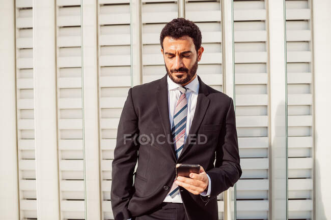 Portrait d'un homme d'affaires barbu portant un costume sombre, vérifiant son téléphone portable. — Photo de stock