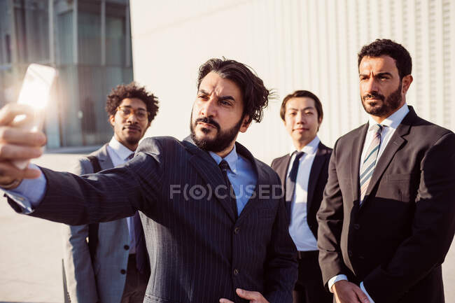 Grupo mixto de hombres de negocios pasando el rato juntos en la ciudad, tomando selfie con teléfono móvil. - foto de stock