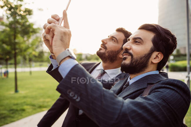 Двое бизнесменов в костюмах стоят на улице, проверяют свои мобильные телефоны. — стоковое фото