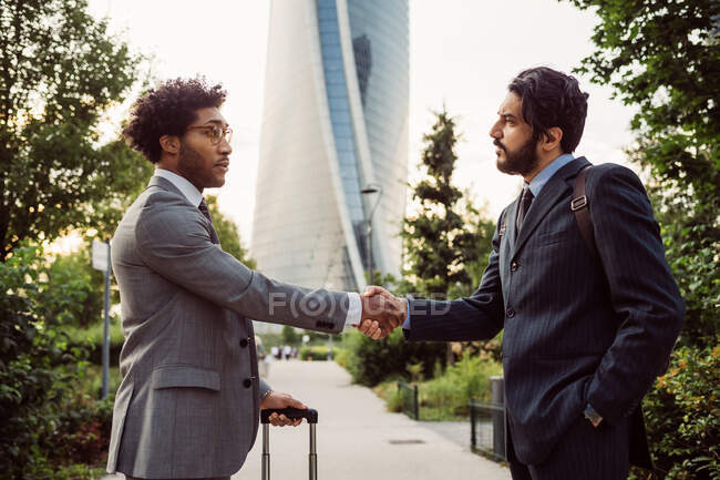 Dois empresários vestindo ternos de pé ao ar livre, apertando as mãos. — Fotografia de Stock