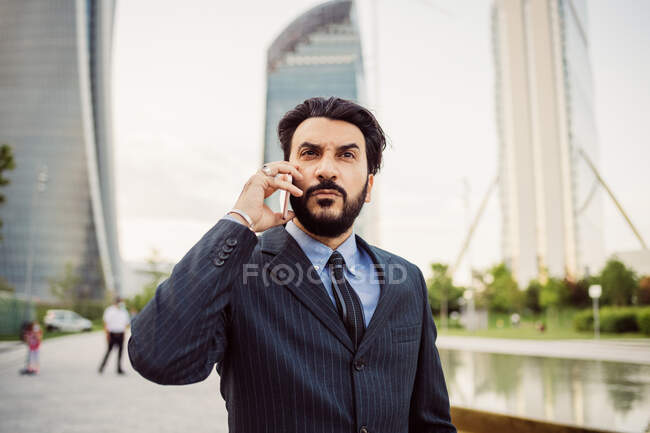 Retrato de empresário barbudo vestindo terno escuro, usando telefone celular. — Fotografia de Stock