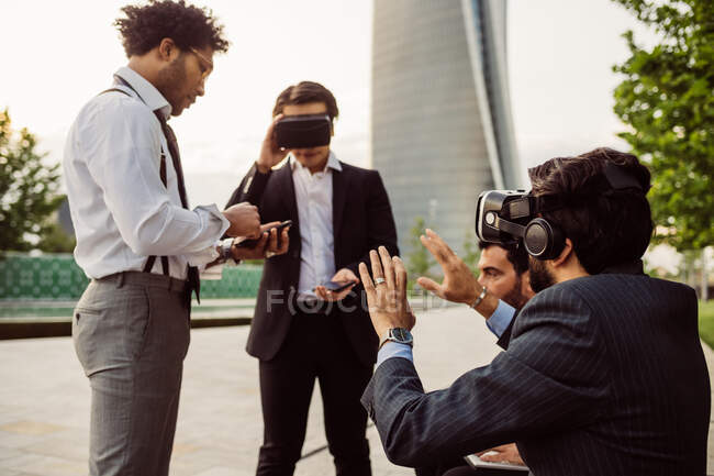 Gruppo misto di uomini d'affari che escono insieme in città, indossando cuffie VR. — Foto stock