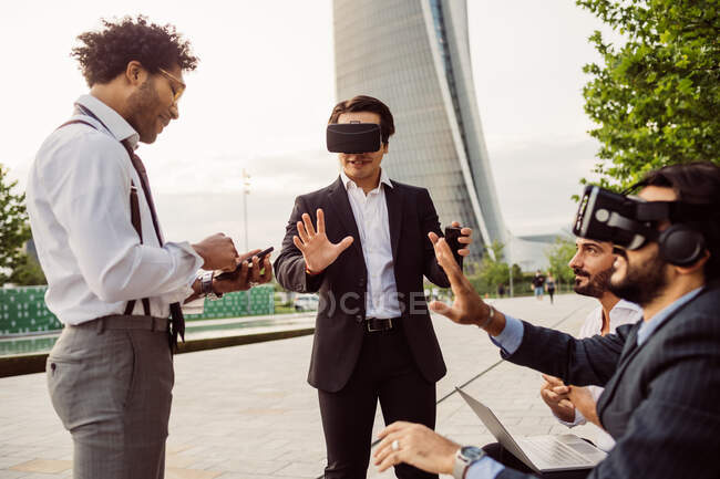 Groupe mixte d'hommes d'affaires qui traînent ensemble en ville, portant des écouteurs VR. — Photo de stock