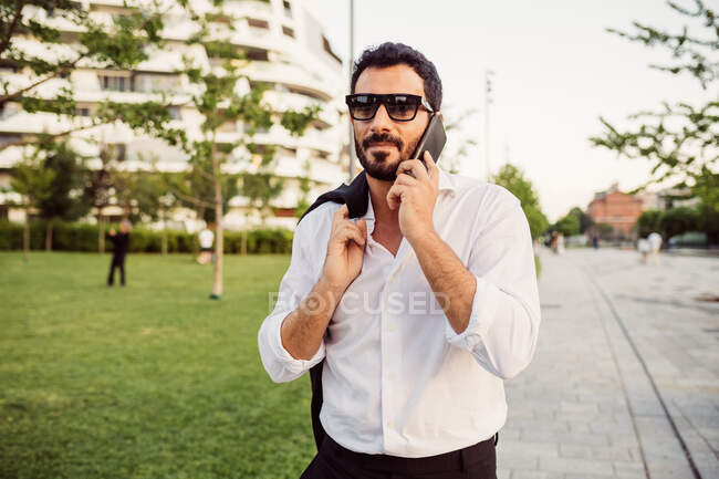 Портрет бизнесмена в белой рубашке и солнцезащитных очках, с помощью мобильного телефона. — стоковое фото