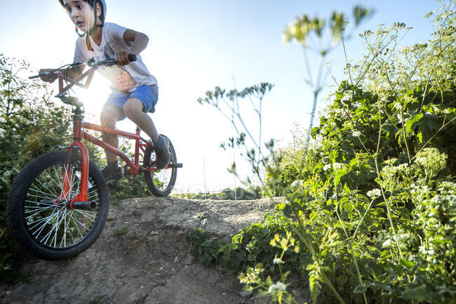 Menino descendo a encosta em uma bicicleta BMX vermelha. — Fotografia de Stock