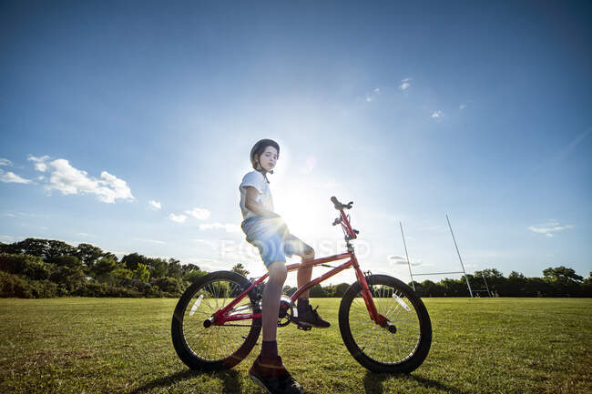 Retrato del niño sentado en su bicicleta BMX, con casco de ciclismo. - foto de stock