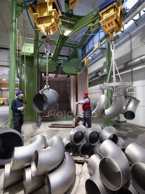 Hombres trabajando en una fábrica de acero, levantando tubos u-bend en cabrestantes. - foto de stock