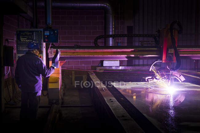 Hombre trabajando en una fábrica de acero, operando soldadora computarizada. - foto de stock