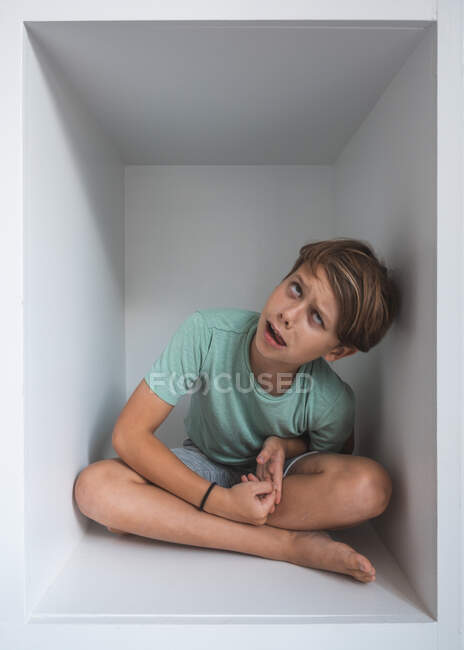 Retrato do menino de cabelos castanhos sentado no armário, olhando para a câmera. — Fotografia de Stock