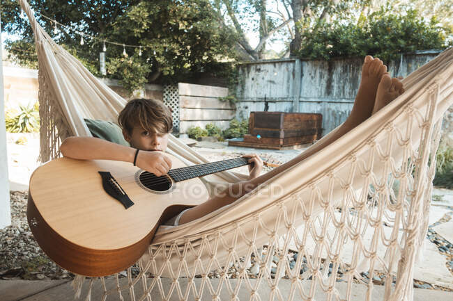 Ragazzo dai capelli castani sdraiato su un'amaca, che suona la chitarra. — Foto stock
