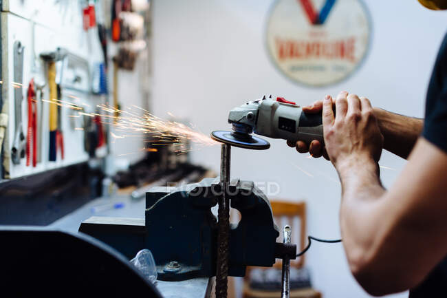 Young man using angle grinder on metal in workshop, cropped — Stock Photo