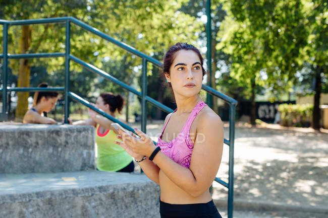 Женщина, использующая мобильный телефон в парке, друзья, отдыхающие на заднем плане — стоковое фото