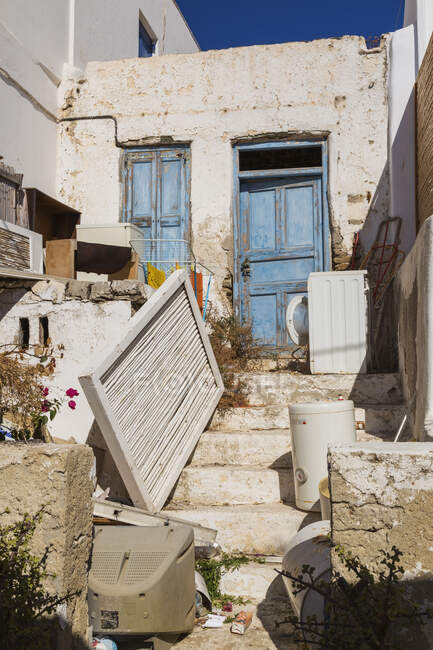 Weggeworfene Gegenstände im Vorgarten eines verlassenen traditionellen Hauses mit blauer Holzeingangstür, Mykonos-Stadt, Insel Mykonos, Griechenland. — Stockfoto
