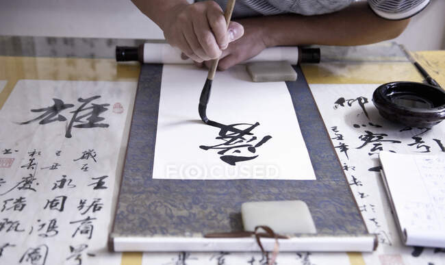 Calígrafo escribiendo símbolos chinos en pergamino - foto de stock