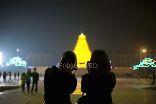 Two Chinese tourists taking photos of the illuminated pagoda in the centre of Sanjiang, Guangxi Provence, China — Stock Photo