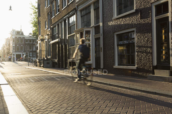 Cyclist riding through cobbled street, Amsterdam, Netherlands — Stock Photo
