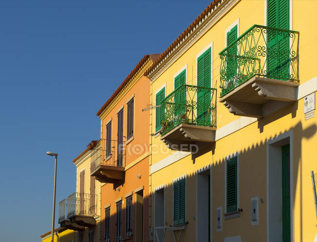 Façade de maison jaune avec balcons et volets verts, Sardaigne, Italie — Photo de stock