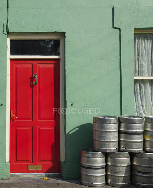 Barriles de cerveza apilados fuera de la casa con puerta roja, Irlanda - foto de stock