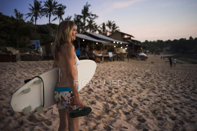 Женщина держит доску для серфинга, глядя на море, Баланган, Бали, Индонезия — стоковое фото