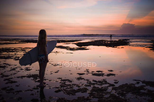 Femme tenant une planche de surf, regardant vers la mer, coucher de soleil, Balangan, Bali, Indonésie — Photo de stock
