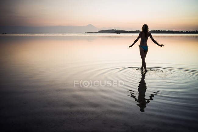Woman standing in the sea at sunset, rear view, Gili Air — Stock Photo
