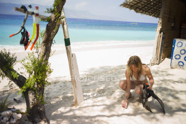 Woman crouching on sand, holding flippers, Gili Air, Indonesia — Stock Photo