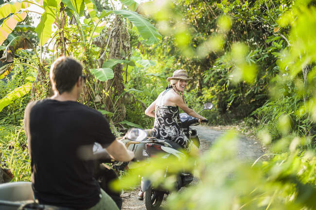 Pareja montando en motocicletas a través del bosque, Nusa Lembongan, Indonesia - foto de stock