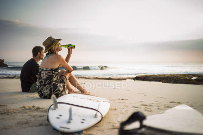 Pareja sentada en la playa con tablas de surf, mirando al mar, Nusa Lembongan, Indonesia - foto de stock