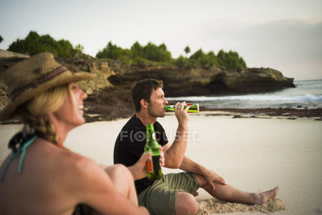 Pareja sentada en la playa, bebiendo cerveza, Nusa Lembongan, Indonesia - foto de stock