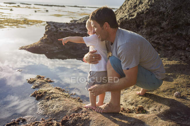 Mann hält kleinen Jungen in der Hand und blickt aufs Meer — Stockfoto