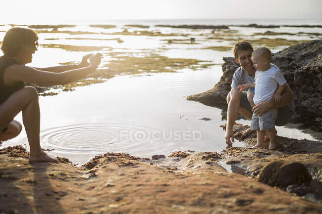 Mother taking photograph of father and son, on beach — Stock Photo