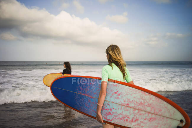 Two woman walking out to sea, carrying surfboards, Seminyak, Bali, Indonesia — Stock Photo