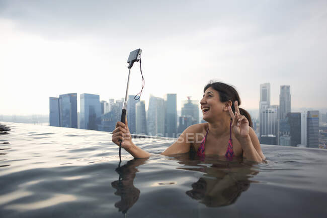 Mujer madura turista tomando selfie smartphone en la piscina infinita, - foto de stock