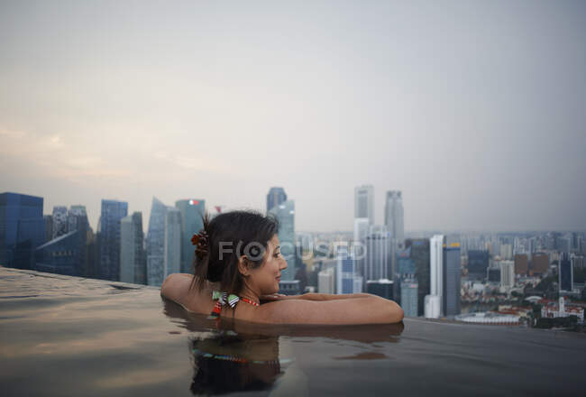 Turista femenina madura mirando desde la piscina infinita del hotel, Sing - foto de stock