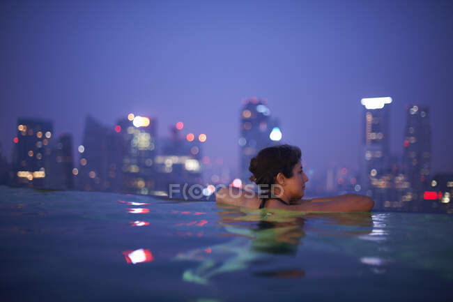 Mature female tourist looking out from hotel infinity pool at ni — Stock Photo