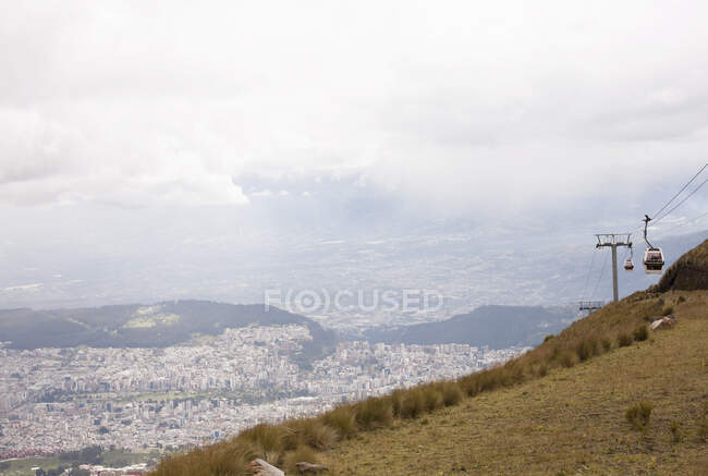 Vista del teleférico subiendo montaña con paisaje urbano lejano, Cruz loma - foto de stock