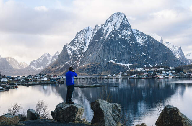Vista trasera del turista masculino fotografiando la montaña nevada y - foto de stock