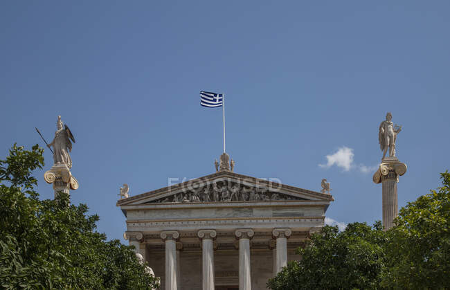 Vista de baixo ângulo da bandeira grega sobre a Academia de Atenas, Atenas — Fotografia de Stock