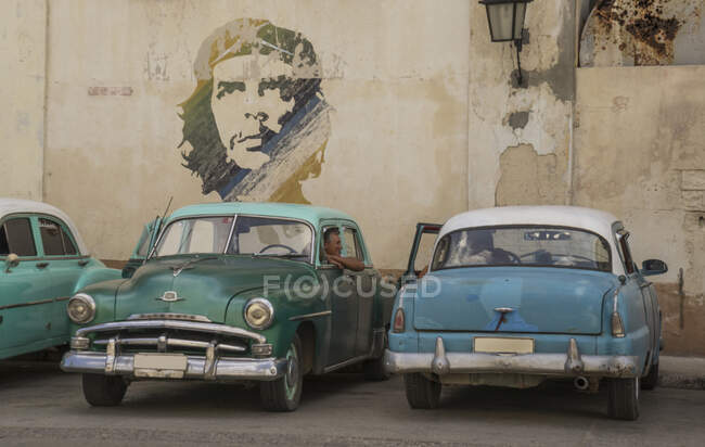 Vintage cars parked under portrait of Che Guevara, Havana, Cuba — Stock Photo