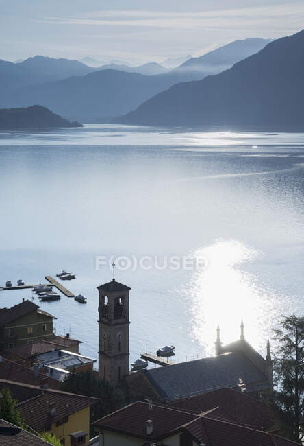 Pueblo frente al mar y montañas lejanas al amanecer, Lago de Como - foto de stock