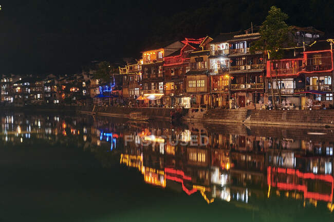 Prédios tradicionais à beira do rio, iluminados à noite, Fenghuang — Fotografia de Stock