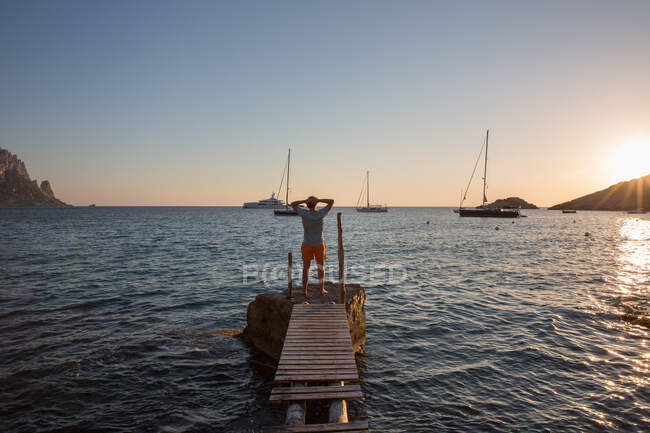 Young man standing on old pier at sunset, Ibiza, Spain — Stock Photo